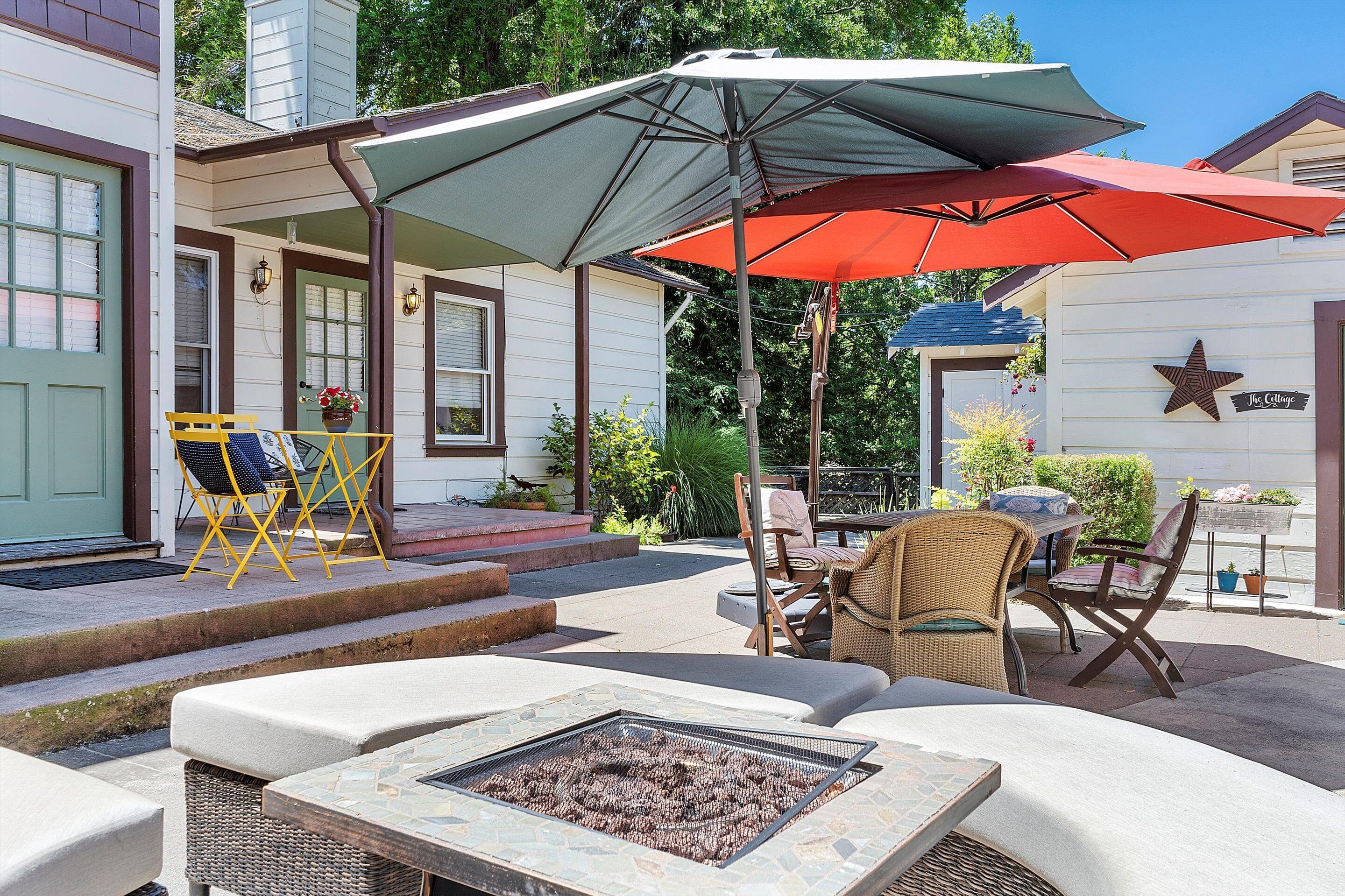 An outdoor patio with a fire pit, outdoor seating, and umbrellas providing shade.