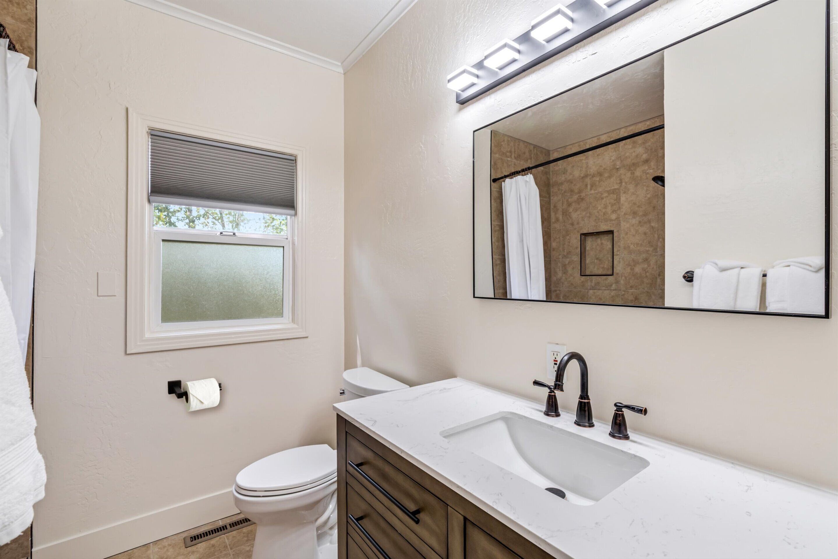 Une salle de bain moderne avec un lavabo blanc, un robinet foncé et un grand miroir au-dessus.