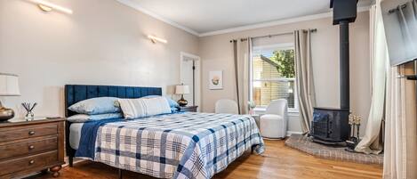Un dormitorio con cama, cómoda, mesita de noche, lámpara y estufa de leña.