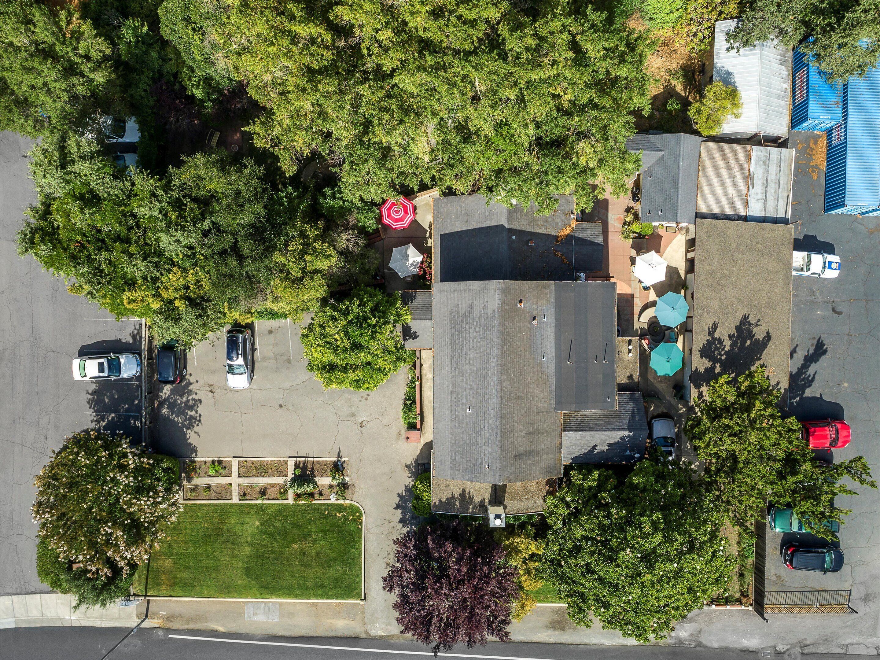 Vista aerea di un parcheggio con diverse auto, alberi e un edificio con tetto spiovente.