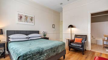 A bedroom with a bed, a chair, a nightstand, a lamp, and a bathroom visible through an open door.