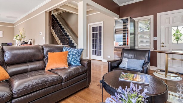 A spacious living room with a brown leather sofa, a coffee table, and a black armchair. A staircase leads to an upper level.