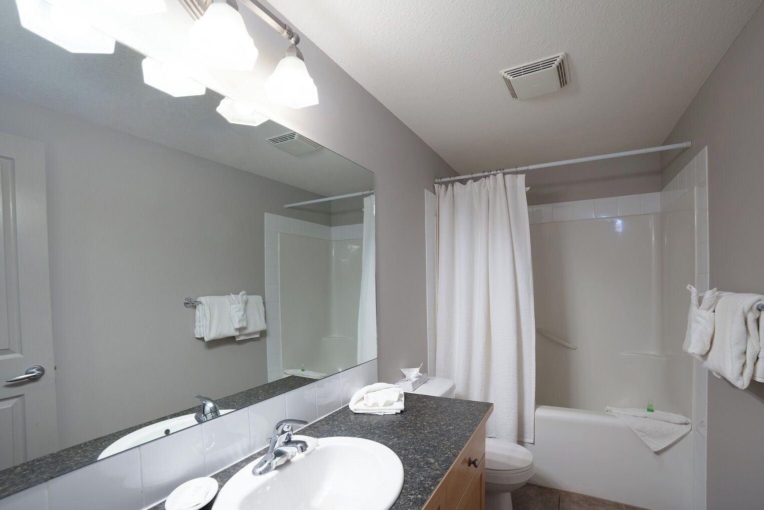 A modern bathroom with a granite countertop sink, a large mirror, a shower with a curtain, and white towels.