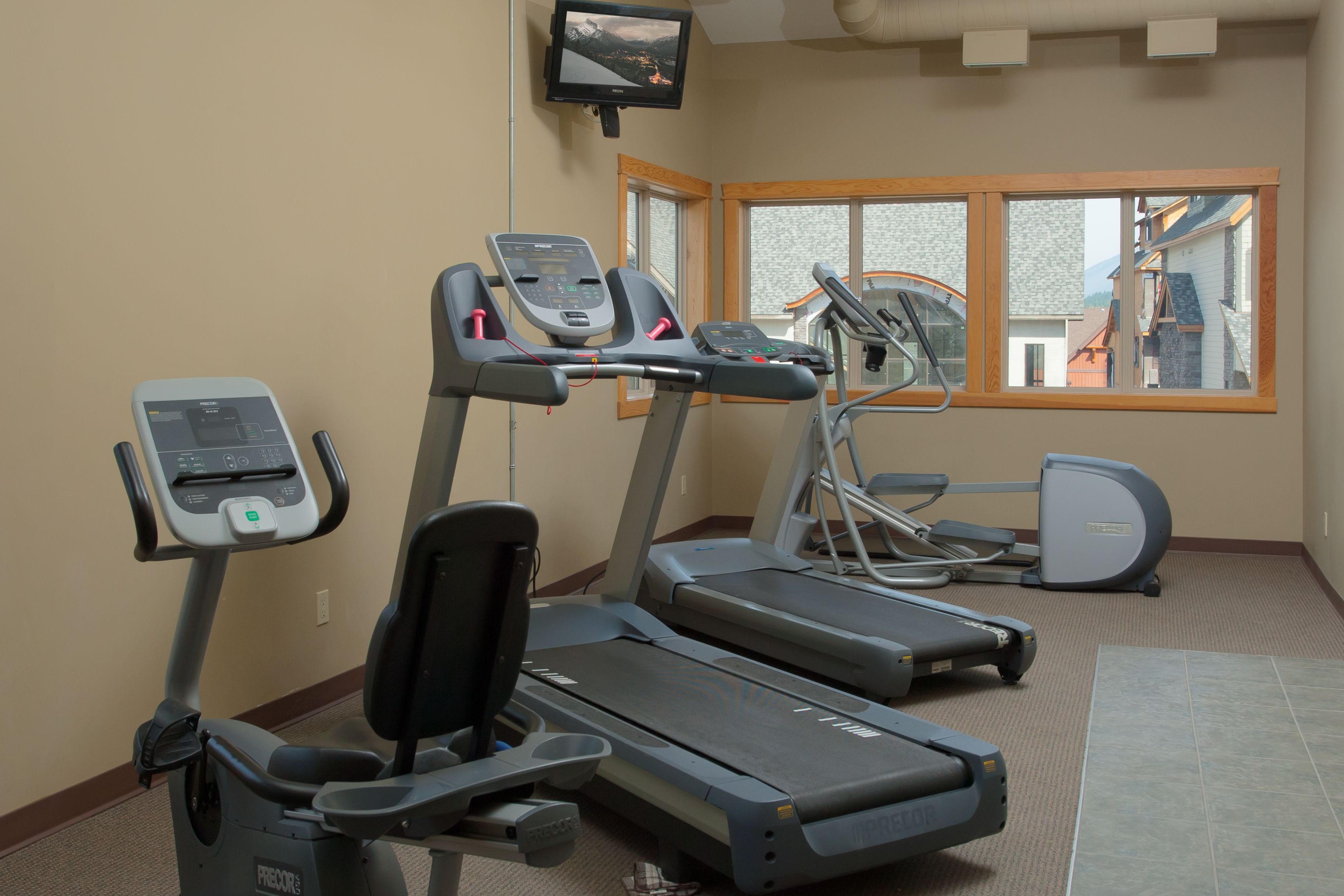 A fitness room with treadmills, a stationary bike, and a TV screen.
