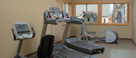 Un gimnasio con cintas de correr, una bicicleta estática y una pantalla de televisión.