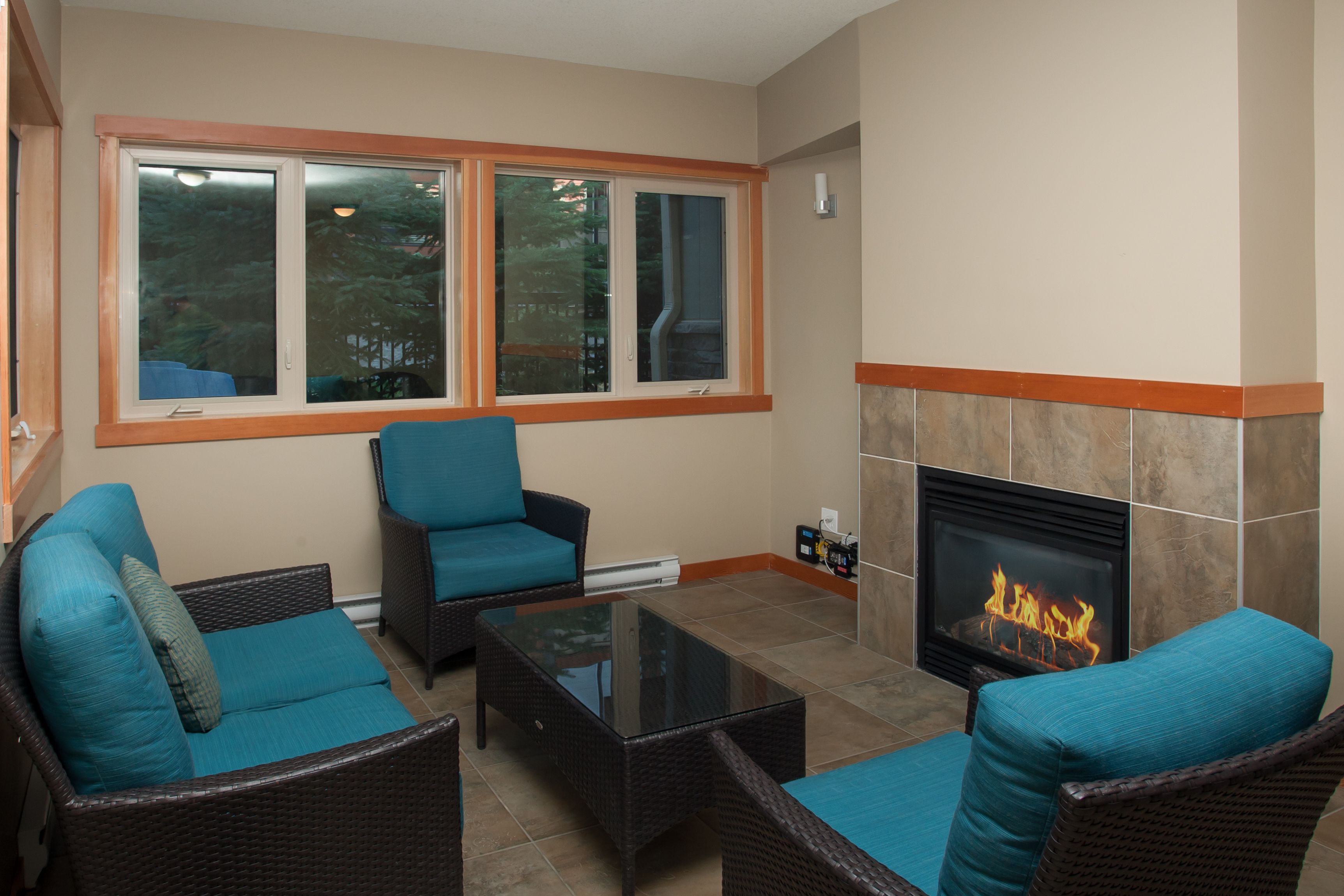 Una sala de estar con muebles de mimbre, chimenea y ventanas amplias.
