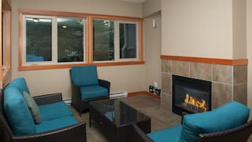 Una sala de estar con muebles de mimbre, chimenea y ventanas amplias.