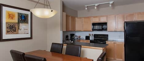 Una cocina moderna con armarios de madera, un refrigerador negro, un microondas y un comedor con mesa y sillas.