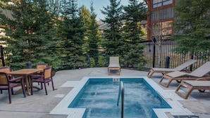 Una piscina rectangular con una escalera de metal, rodeada de sillas de descanso y una mesa de madera con sillas.