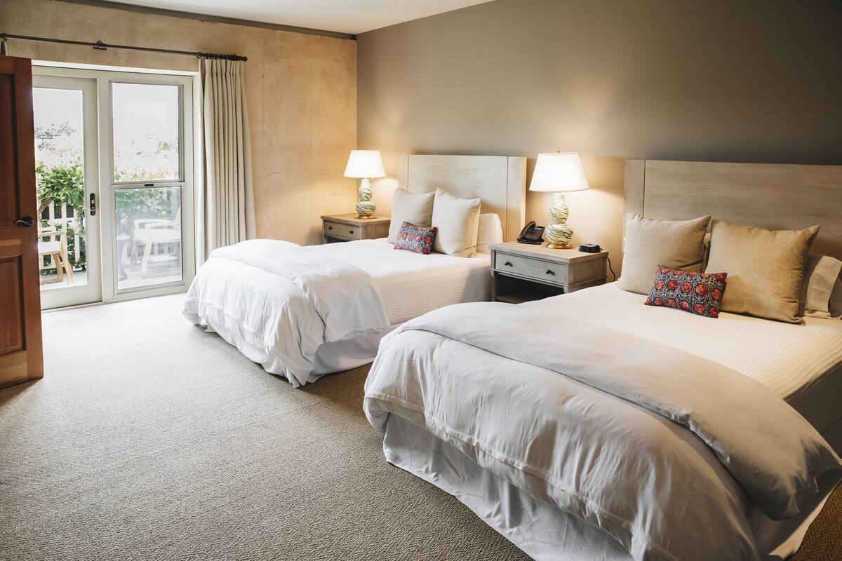 A hotel room with two beds, a sliding glass door to the balcony, and a nightstand with a lamp and phone.