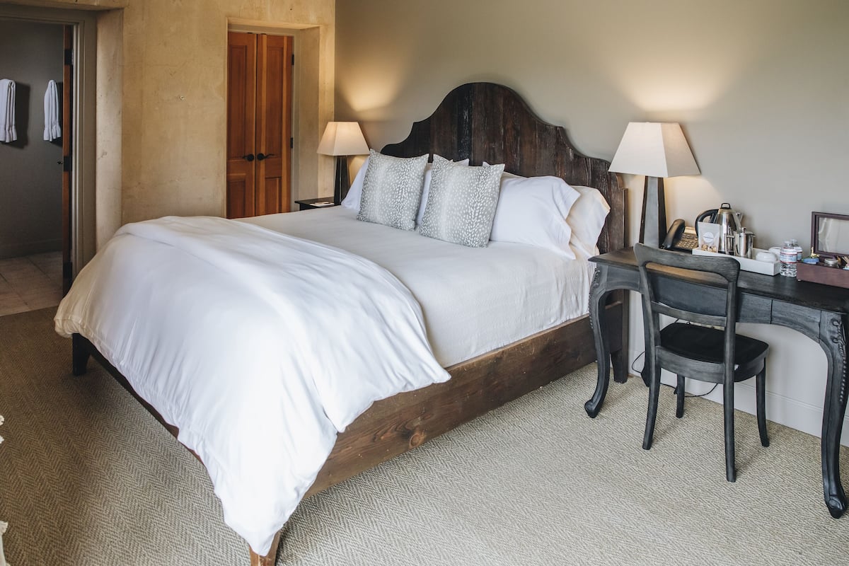 A neatly made bed with white linens, a wooden headboard, and two bedside lamps.
