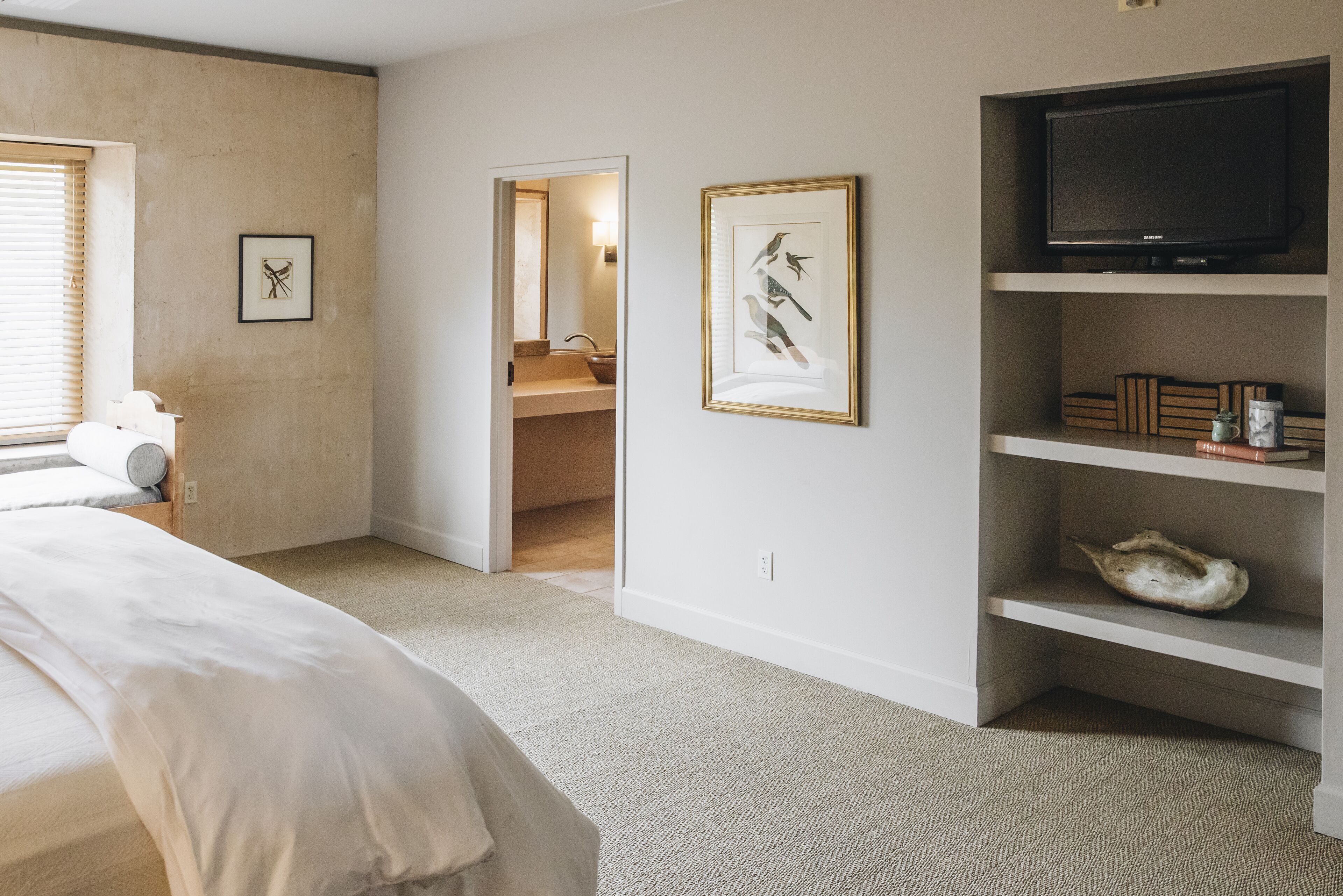 A bedroom with a bed, a television, and a bathroom visible through an open door.