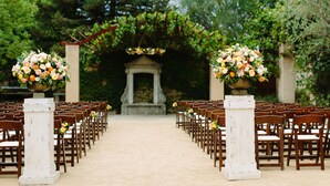 An outdoor venue with rows of wooden chairs and white columns, each topped with a floral arrangement. - Seven Branches Venue and Inn (Sonoma)