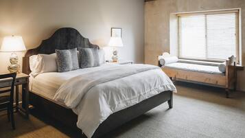 A bedroom with a bed, two bedside tables with lamps, a window with blinds, and a bench by the window.