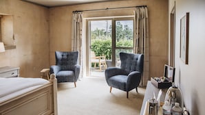 A hotel room with a bed, two armchairs, a small table with amenities, and a sliding glass door leading to an outdoor area. - Seven Branches Venue and Inn (Sonoma)