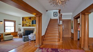 A spacious living room with a wooden staircase, a fireplace, and a chandelier. - Casa Bella (Kenwood)