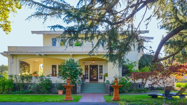 A two-story house with a covered porch, a front door, and a small garden with a fountain. - Casa Bella (Kenwood)