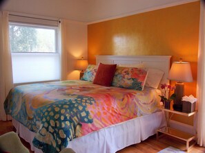 Quarto com uma cama, duas luminárias de cabeceira, mesa de cabeceira, janela e vista para árvores lá fora.