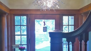 A grand foyer with a chandelier, a wooden staircase, and a view through a large door. - Casa Bella (Kenwood)