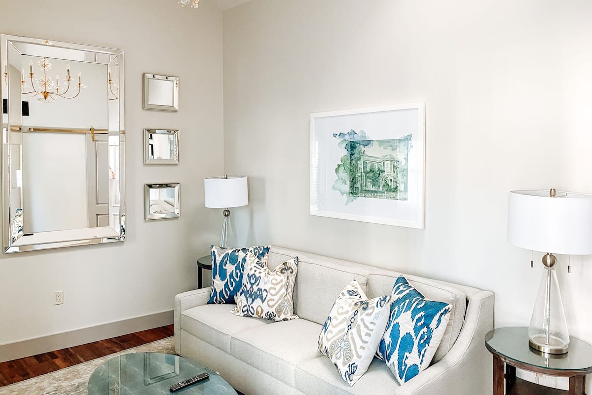 A living room with a sofa, a glass coffee table, a chandelier, a framed picture, and a lamp.