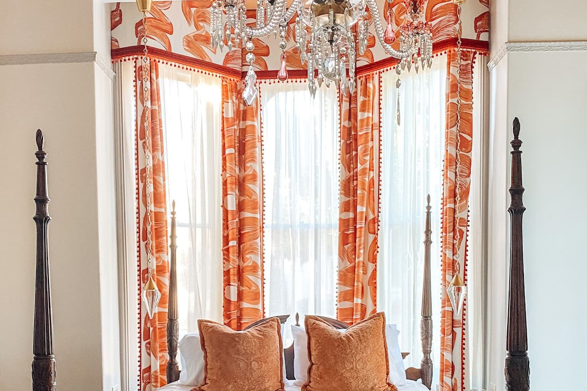 A bedroom with a four-poster bed, ornate curtains, and a chandelier.