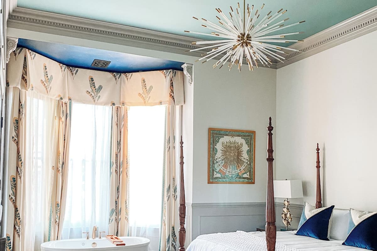 A bedroom with a four-poster bed, a freestanding bathtub, and a large window with curtains.