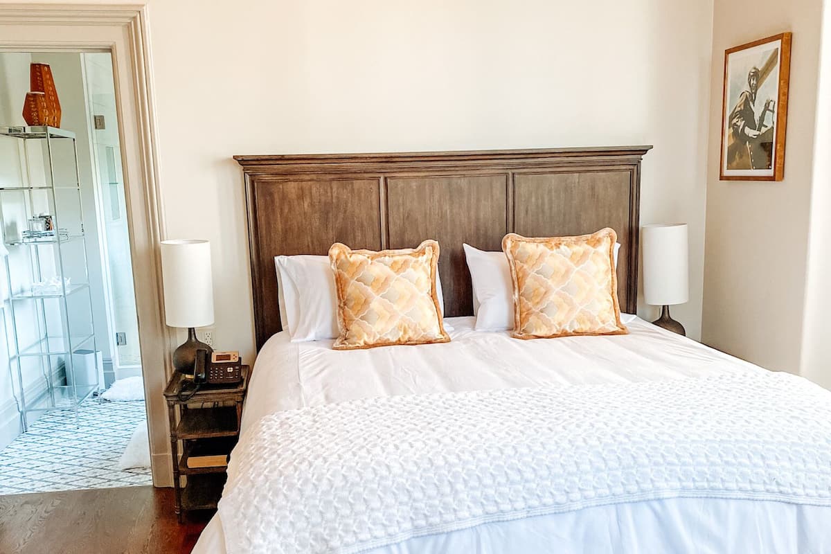 A neatly made bed with a wooden headboard, two bedside lamps, and a book on a side table.