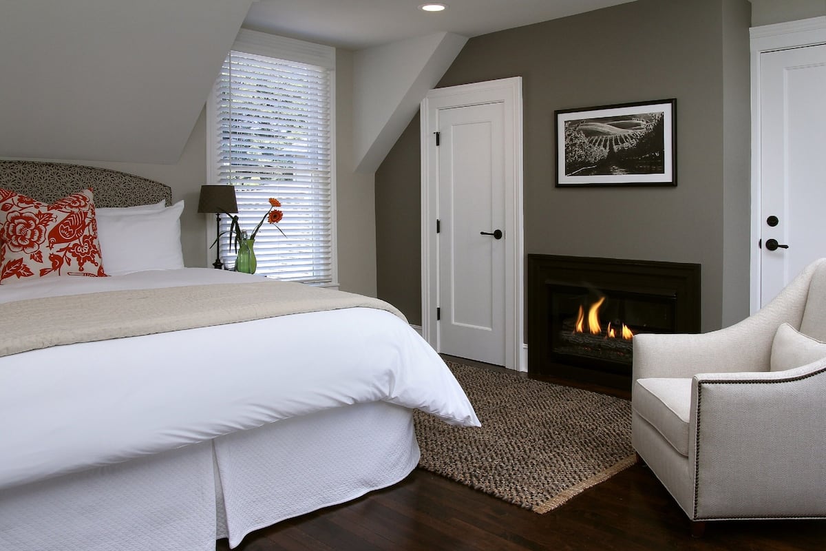 A bedroom with a large bed, a fireplace, and a chair.