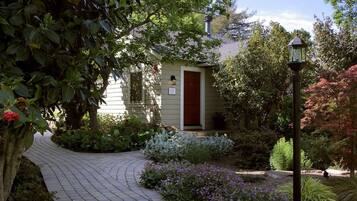 A house with a red door, surrounded by a garden with various plants and a paved pathway.