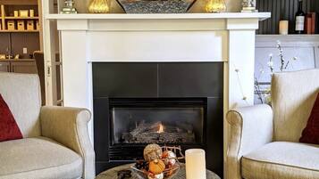 A cozy living room with a fireplace, two armchairs, a round coffee table, and a bookshelf with books and decorative items.
