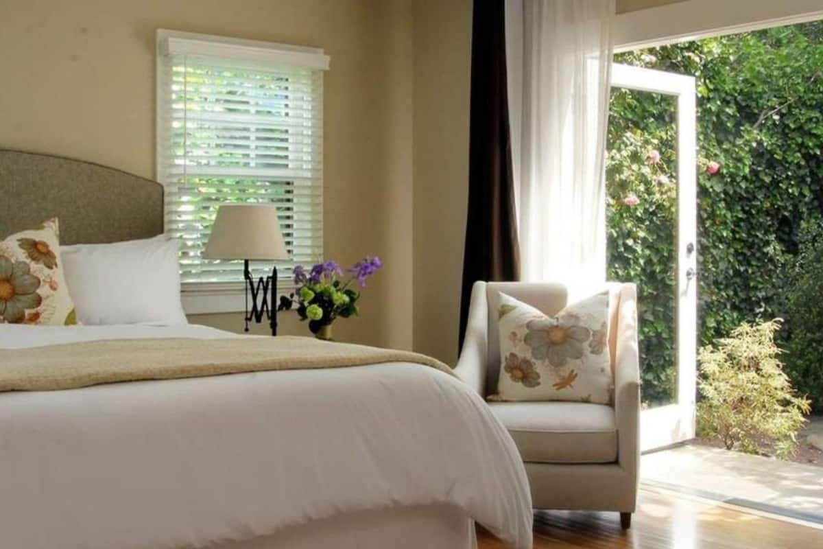 A bedroom with a bed, a chair, a lamp, and a window with blinds.