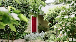 A garden pathway leading to a building with a red door, surrounded by various plants and flowers. - Inn on Randolph (Napa)