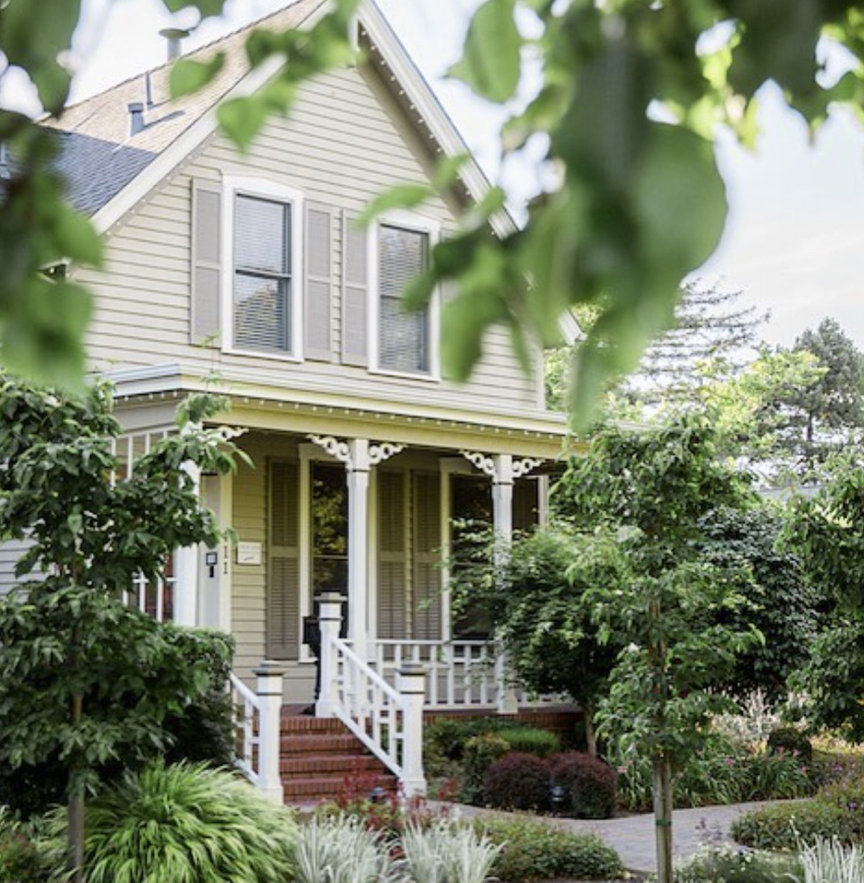 A two-story house with a front porch, a staircase leading to the entrance, and a well-maintained garden.