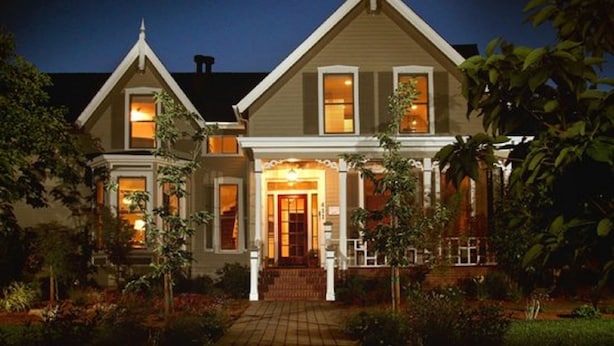 A two-story house with a central entrance, a covered porch, and a well-maintained garden. - Inn on Randolph (Napa)