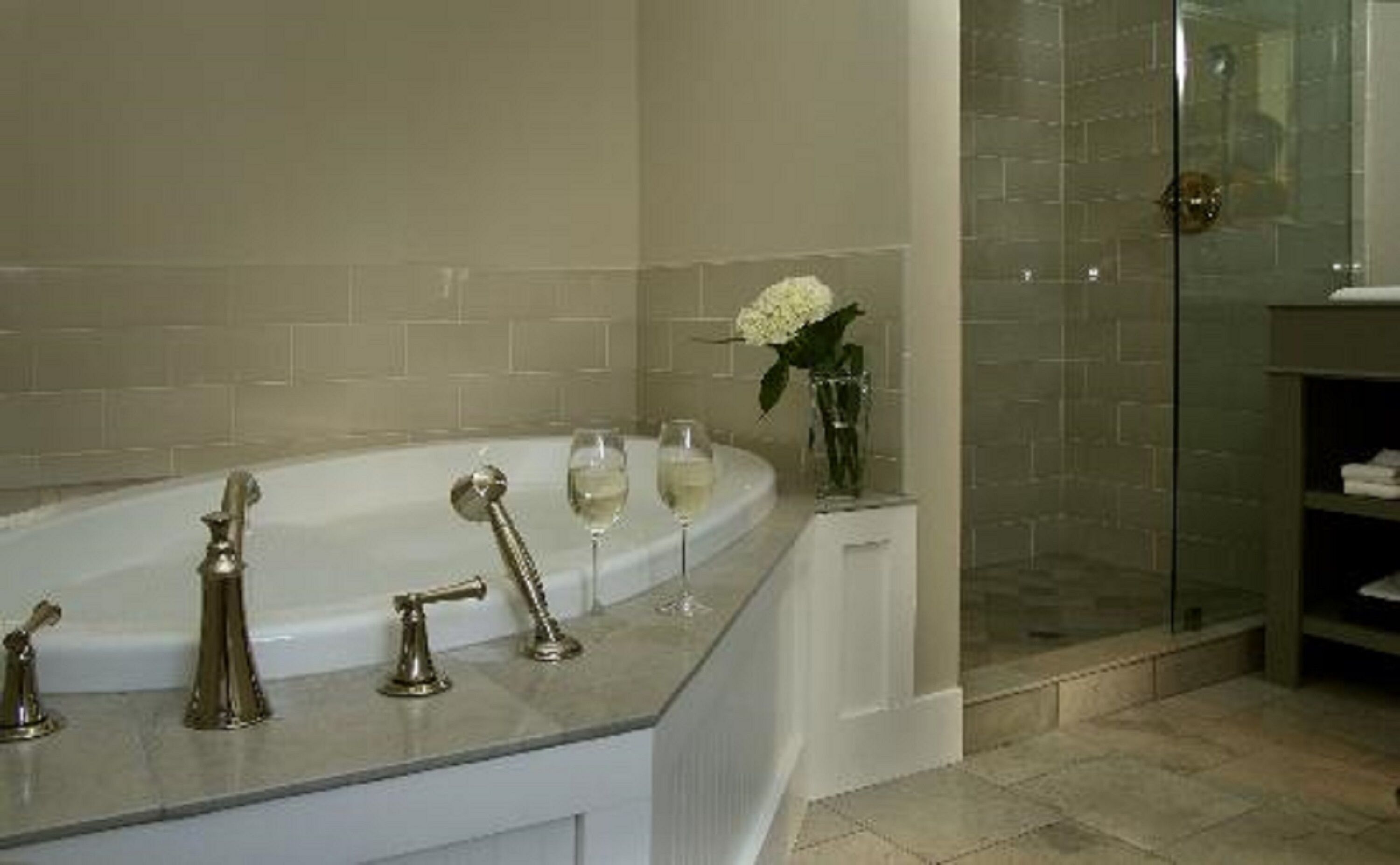 A bathroom with a freestanding bathtub, a glass shower enclosure, and a vase with a flower on the counter.