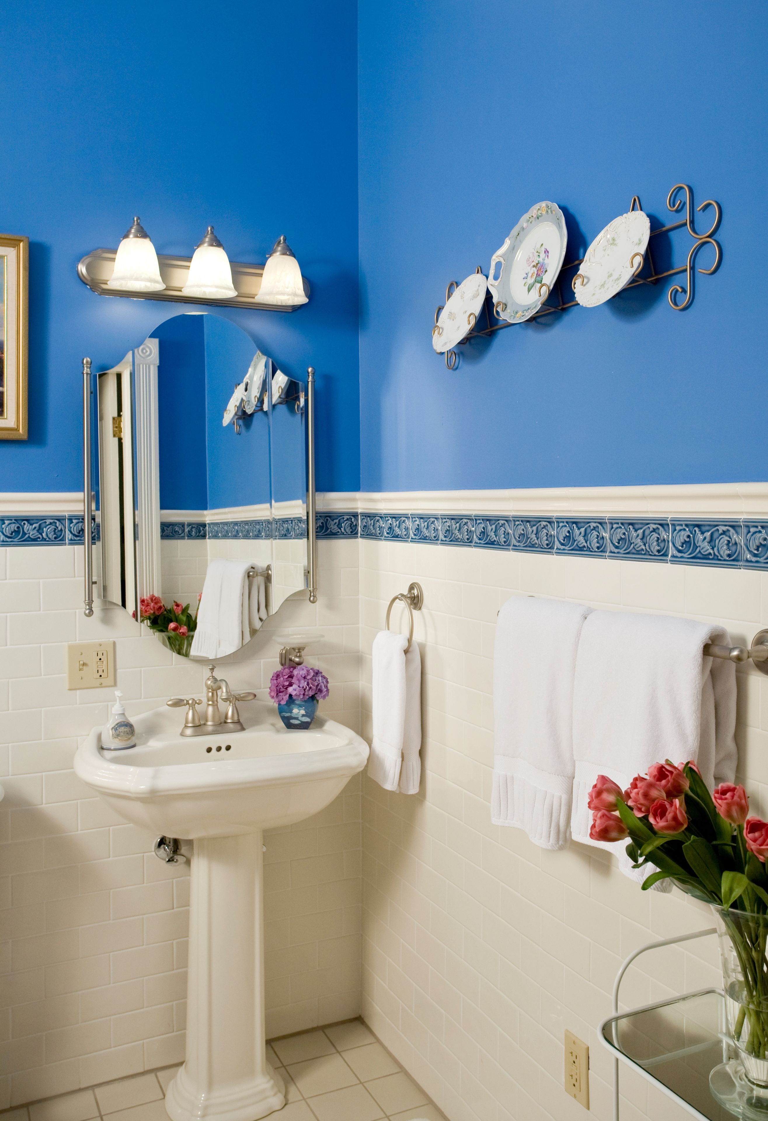 A bathroom with a white sink, a mirror, and a blue wall. There are white towels hanging on the wall and a vase with flowers on the counter.