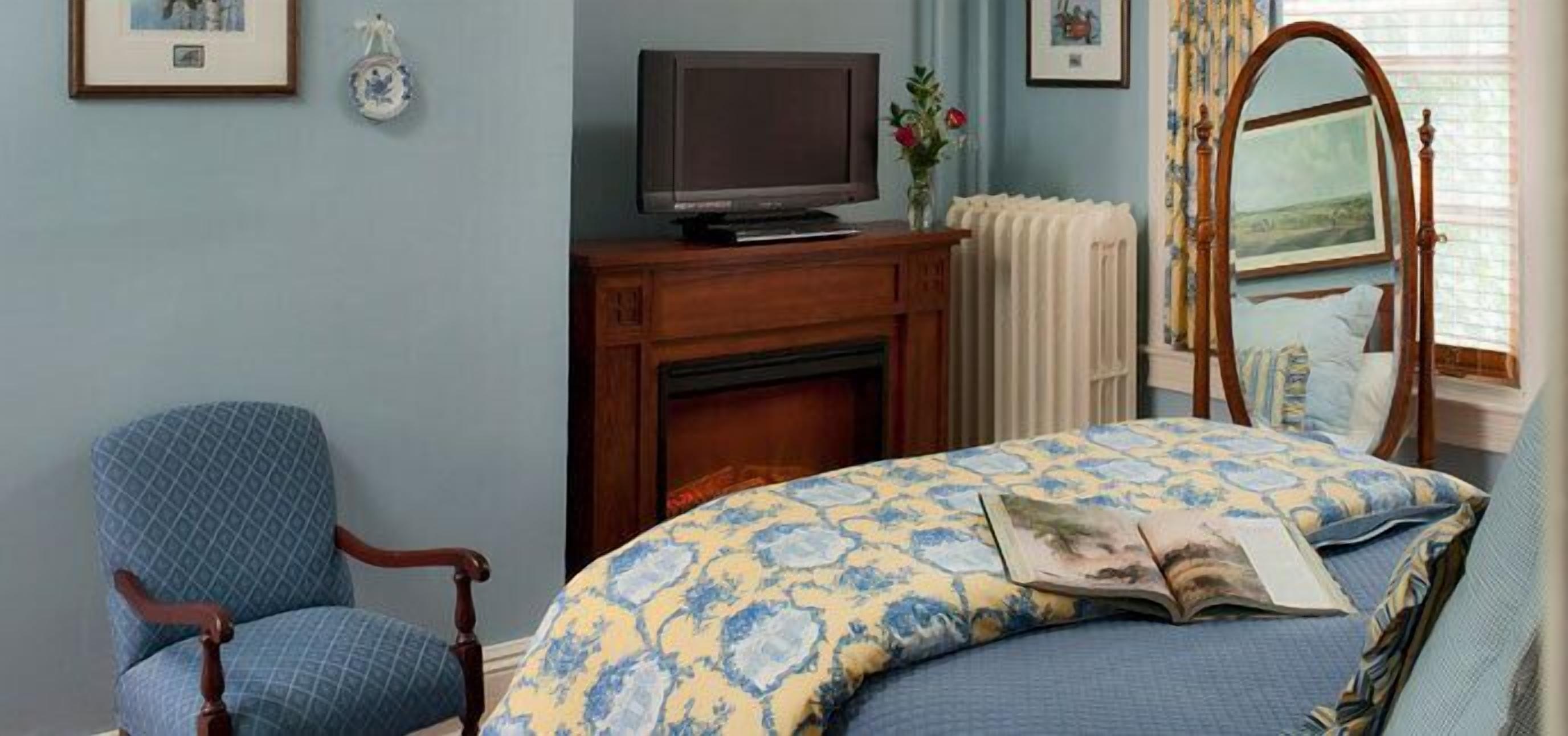 A bedroom with a bed, a chair, a television, and a fireplace.