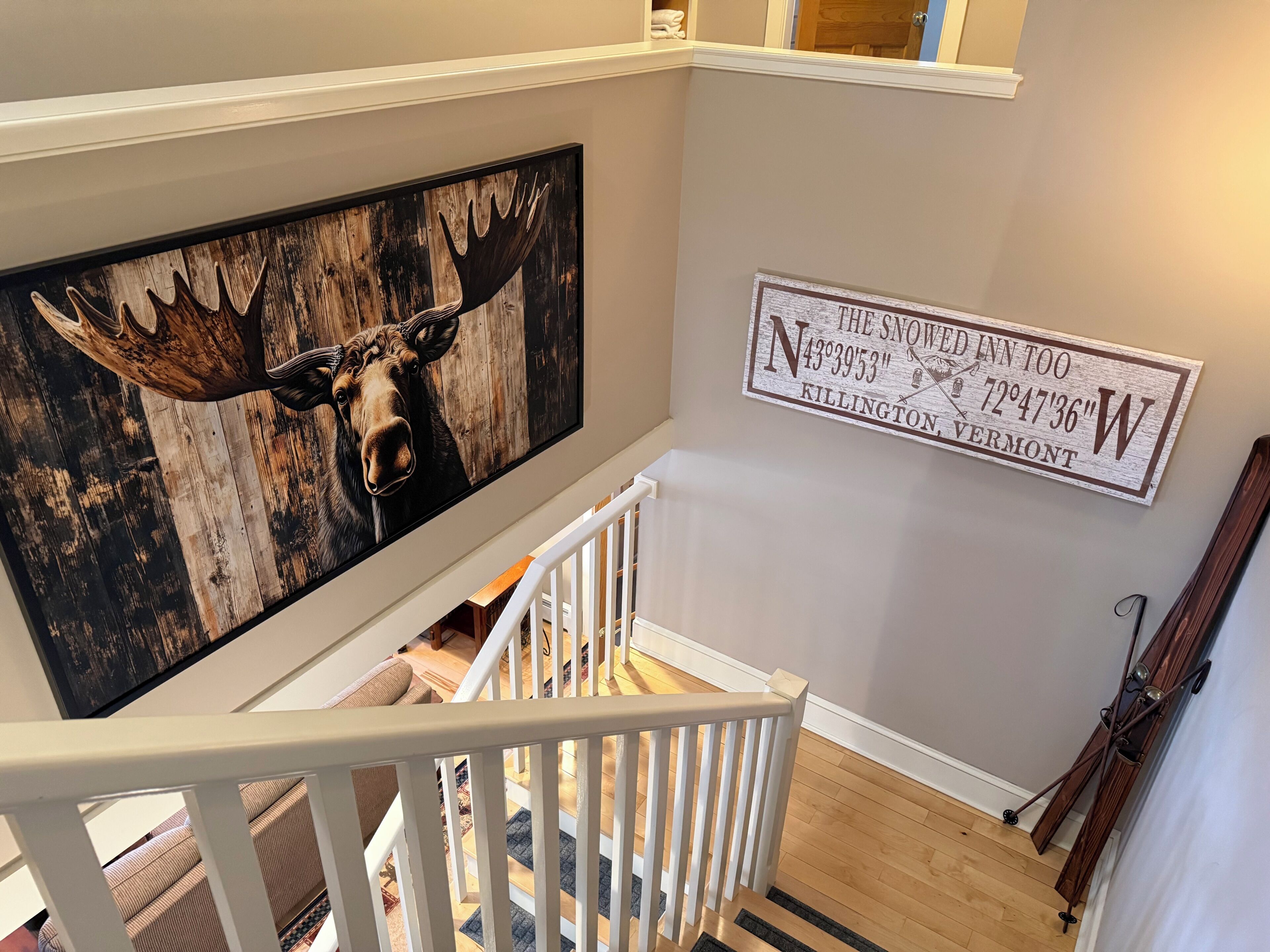A staircase with a wooden railing, a large moose painting, and a sign with coordinates.