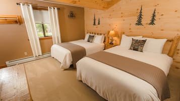 Une chambre confortable, aménagée dans le style d’un chalet, avec deux lits, un mur en bois décoré de motifs d’arbres, une fenêtre avec des rideaux et une petite table.