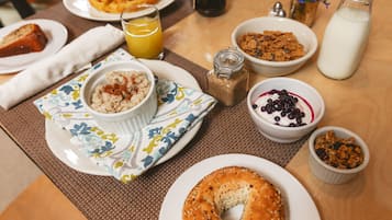 A breakfast table with various food items including a bagel, cereal, and a glass of orange juice.