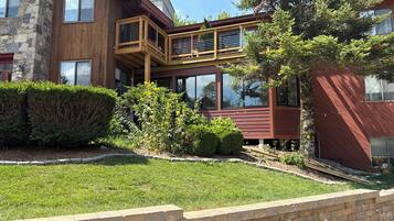 Una casa de dos pisos con un balcón de madera, un muro de piedra y un césped cuidado.