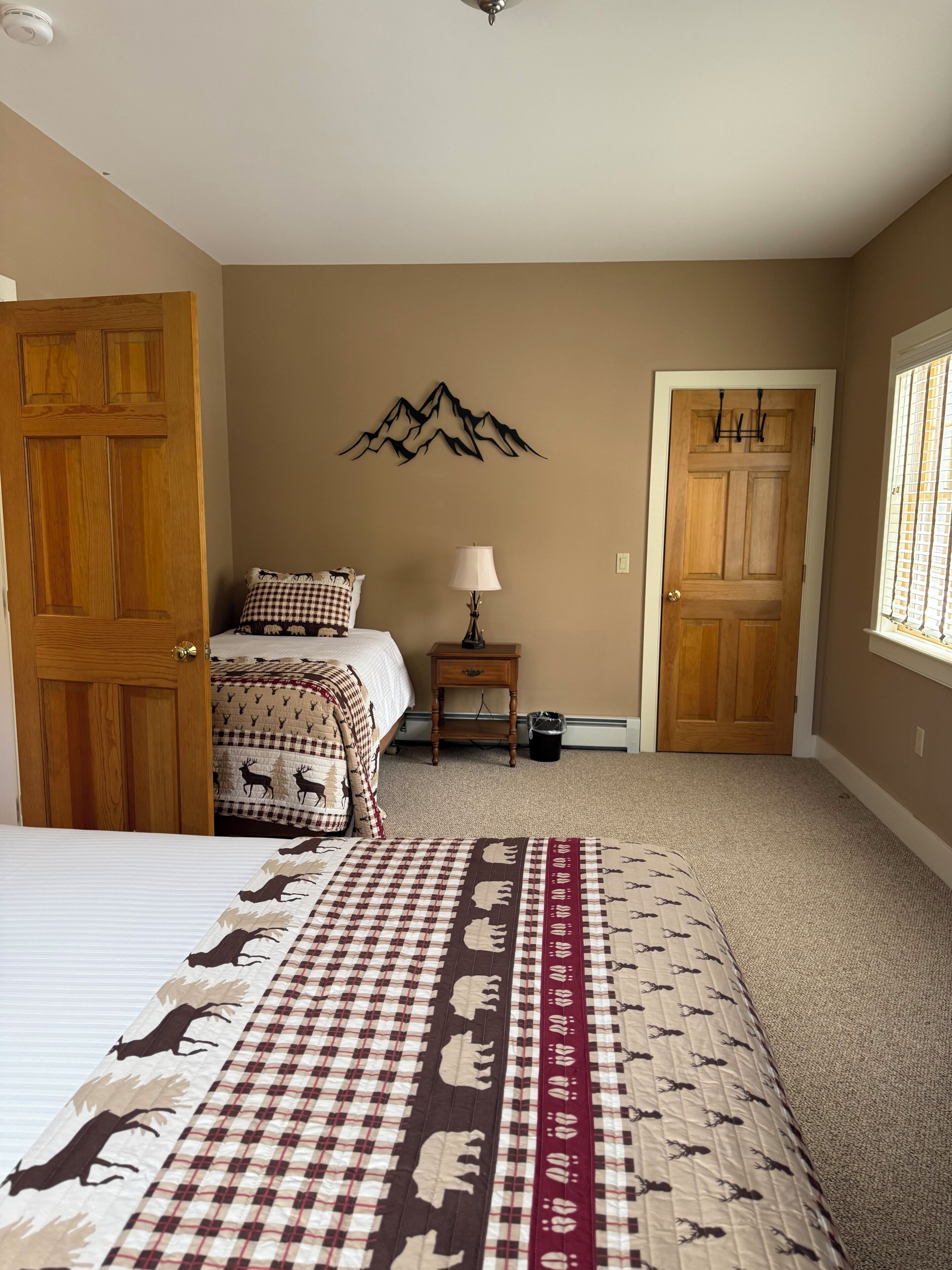 A bedroom with a bed, a nightstand, a lamp, a wall decoration, and two doors.