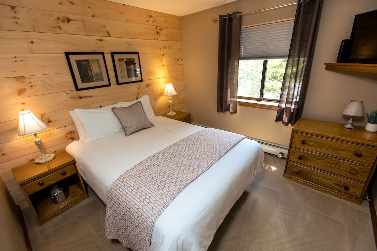 A neatly arranged bedroom with a bed, bedside tables, a dresser, and a window with curtains.