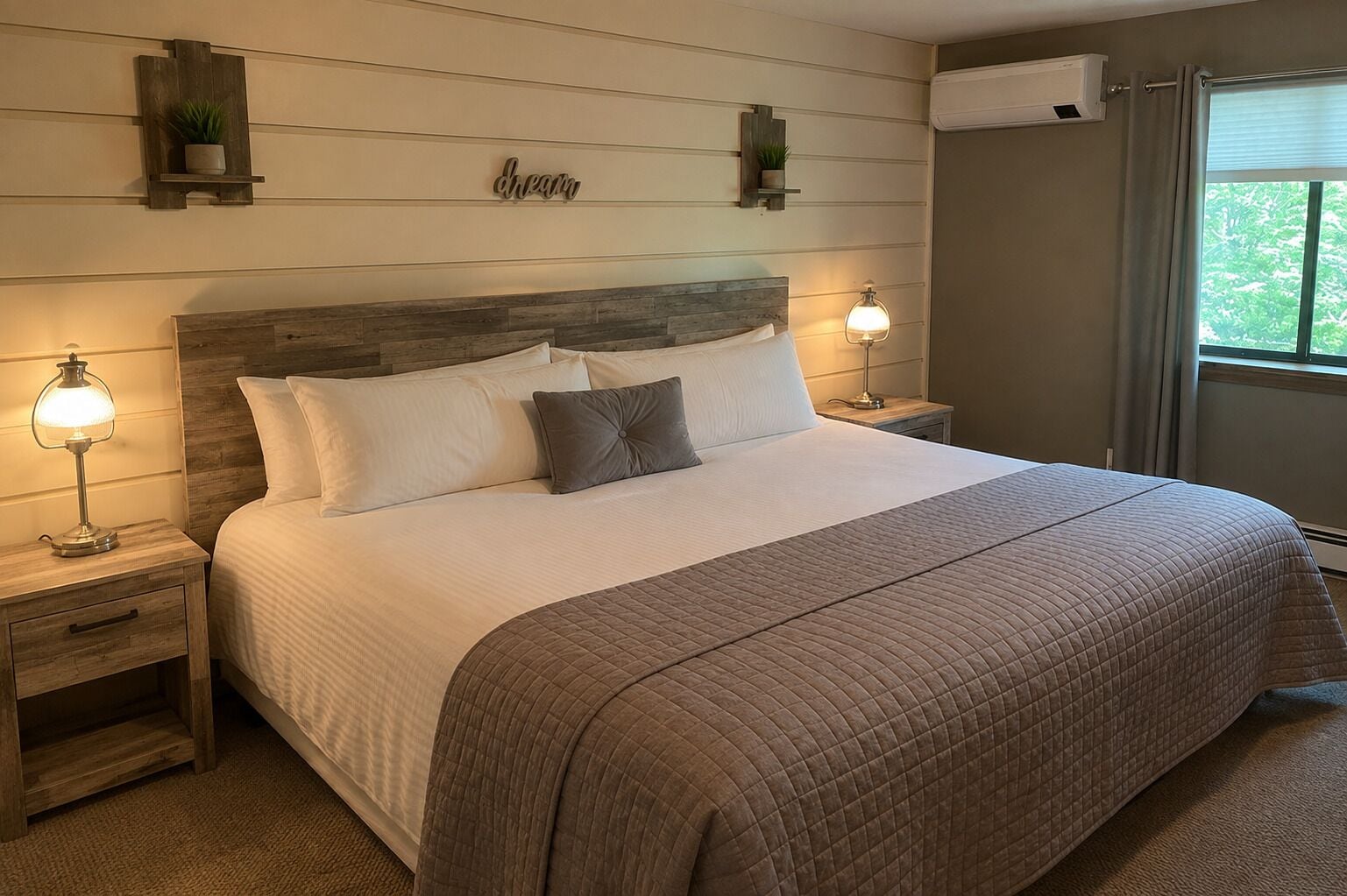 A neatly made bed with a quilted bedspread, two bedside lamps, a nightstand with a drawer, and a wall-mounted shelf with a plant.