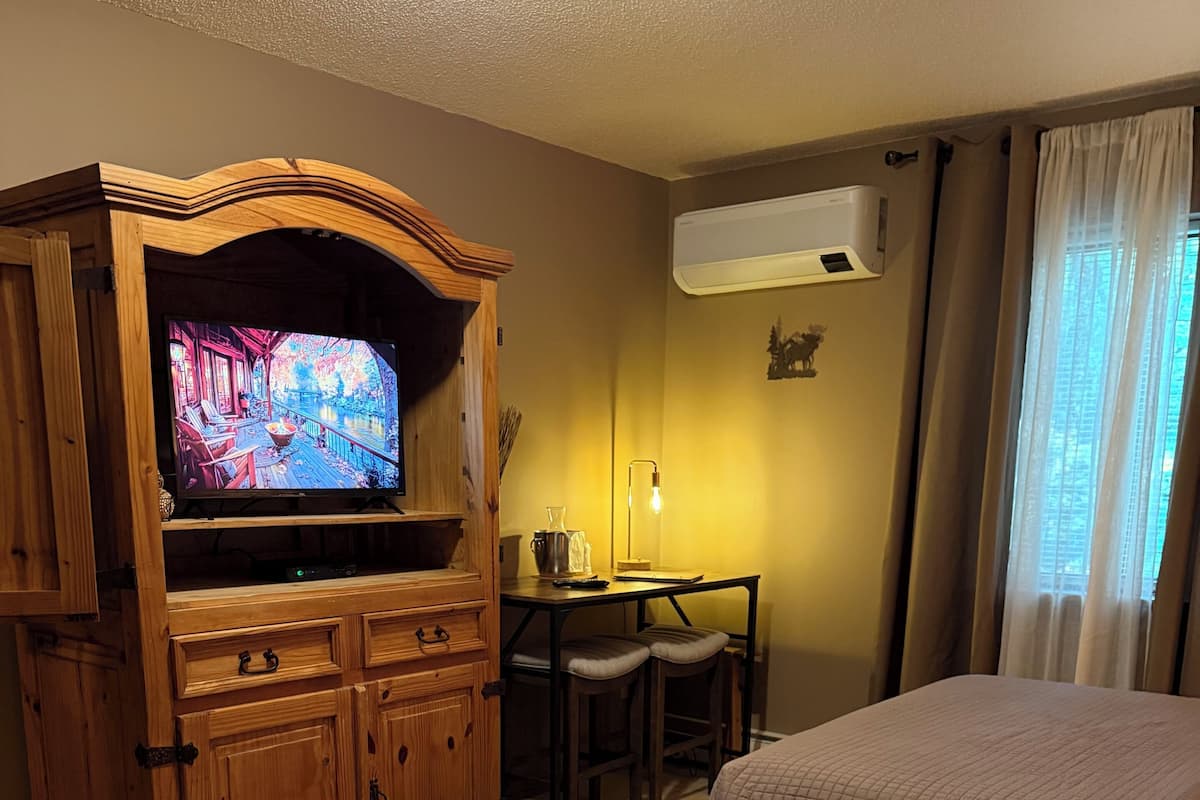 A hotel room with a TV, wooden furniture, a desk with a lamp, and two beds.