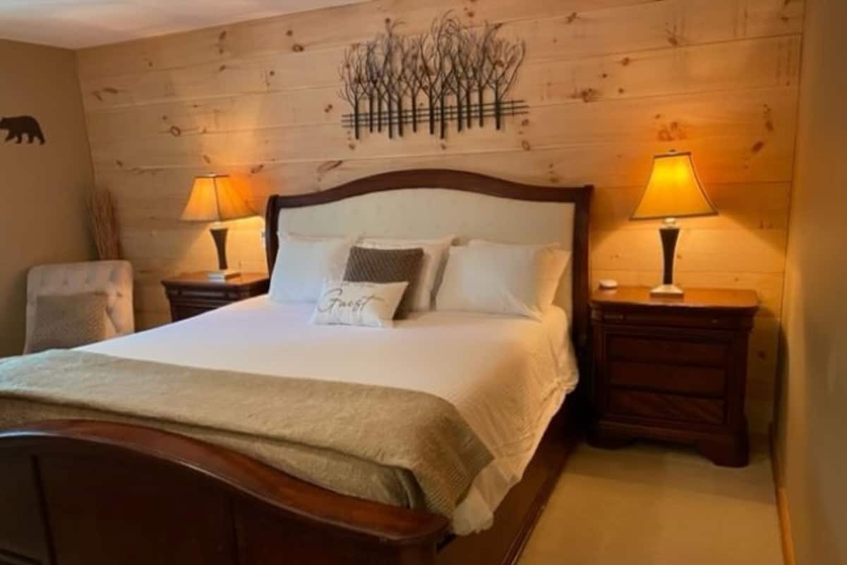 A neatly made bed with a 'Guest' pillow, two bedside lamps, and a wooden headboard.