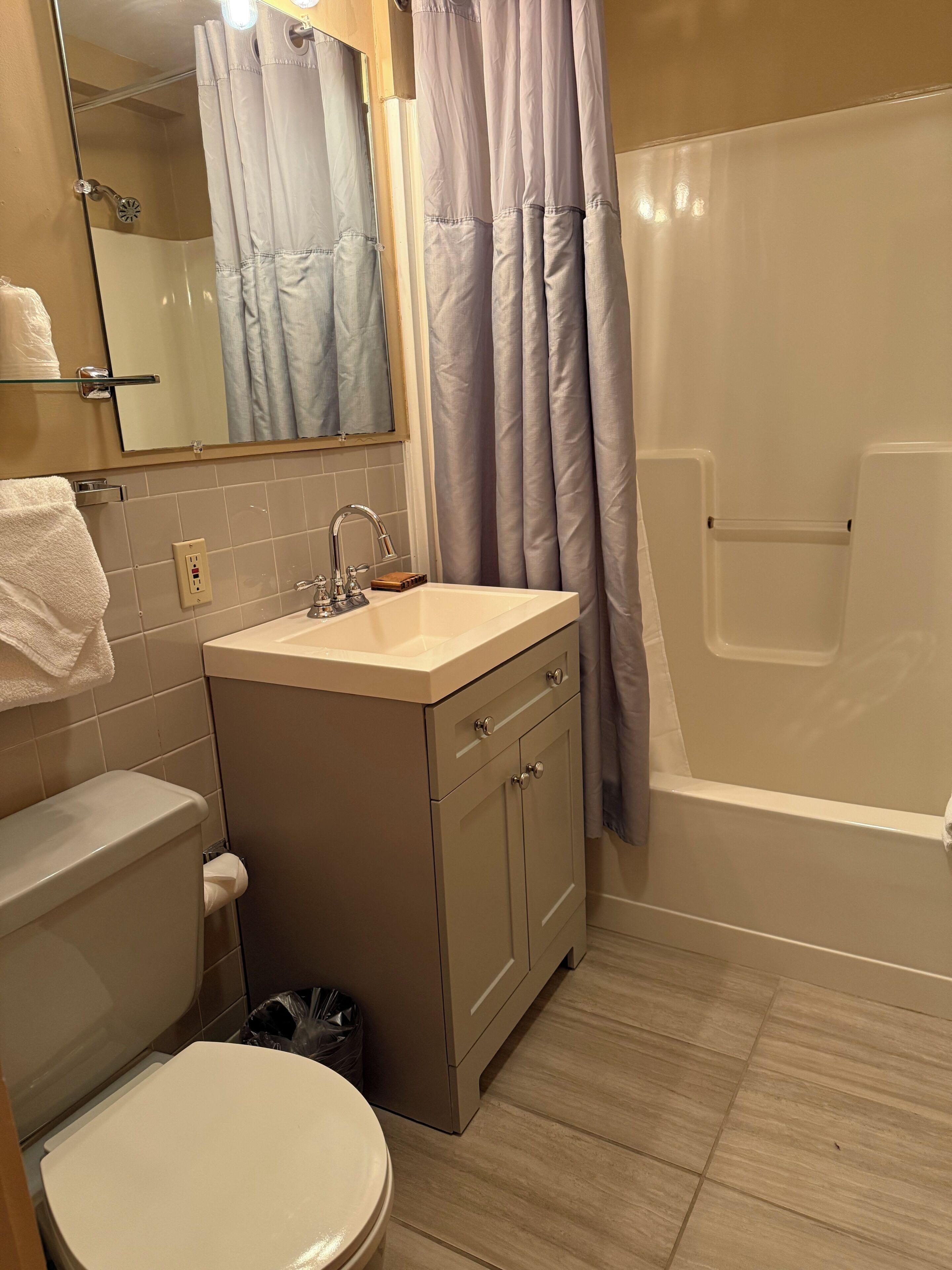 A bathroom with a toilet, sink, mirror, and shower area.