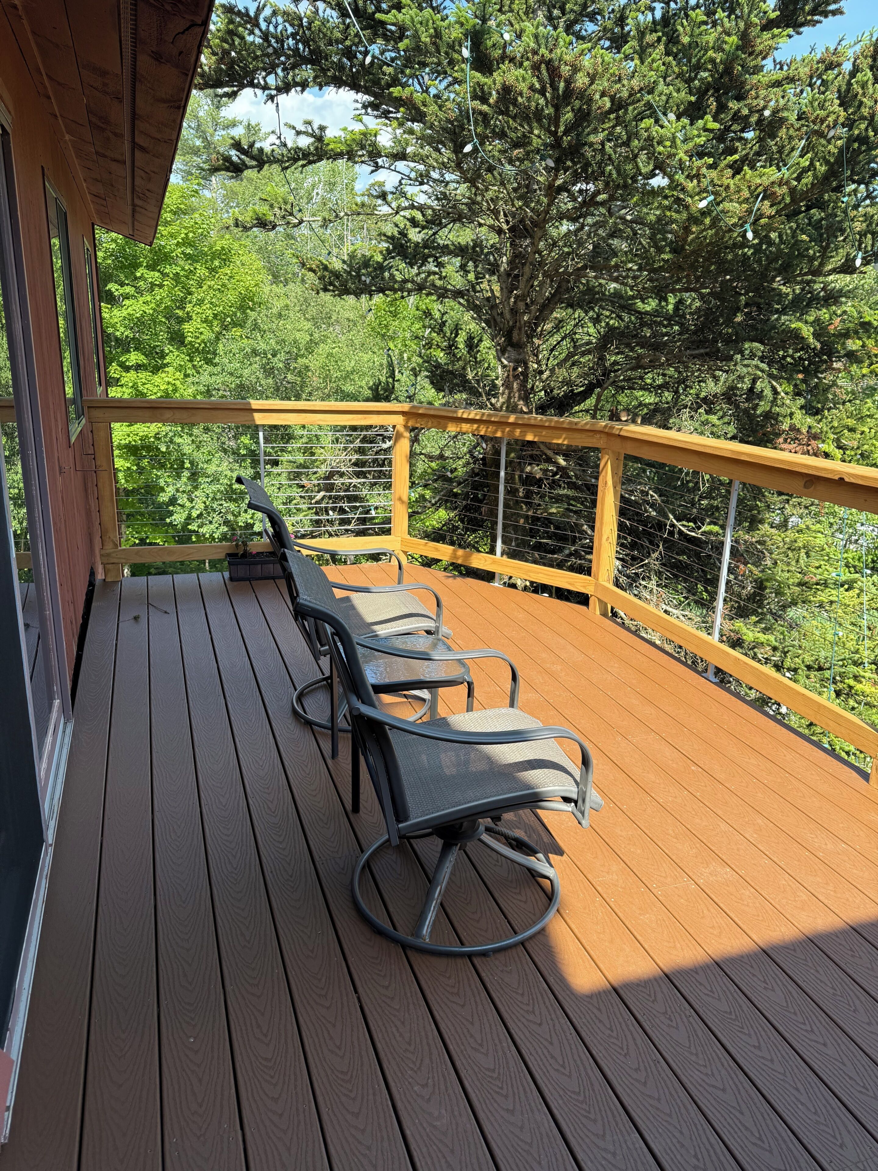 A wooden deck with metal chairs and a railing, overlooking a forested area.