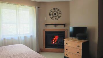 A room with a fireplace, a television on a wooden dresser, and a bed with a pink quilt.