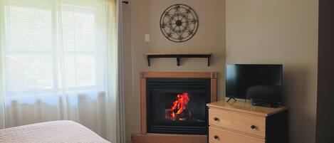 A room with a fireplace, a television on a wooden dresser, and a bed with a pink quilt.